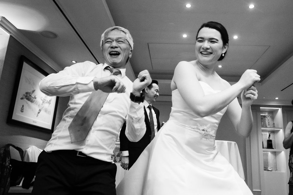 Black and white photo of a bride and older man joyfully dancing together at a wedding reception.