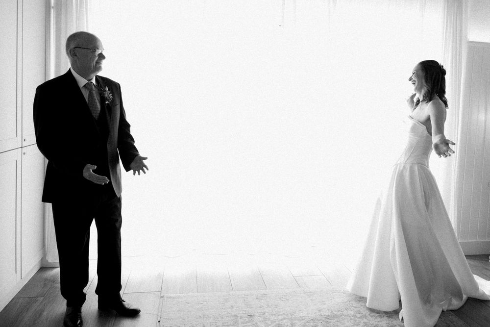 Black and white photo of a bride in a white gown sharing an emotional first look moment with her father.