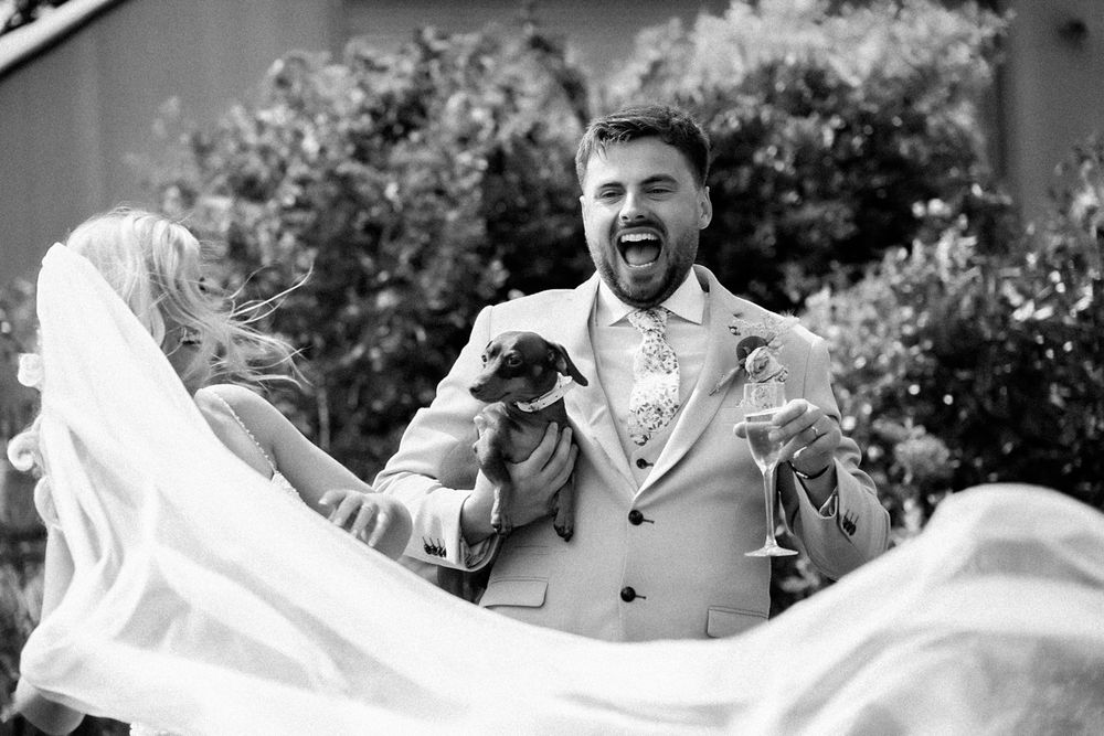 Black and white photo capturing joyful moment with flowing wedding veil outdoors.