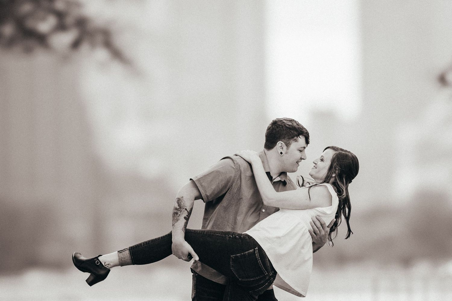 Black and white photo of a romantic couple kissing, man lifting woman in an outdoor urban setting.