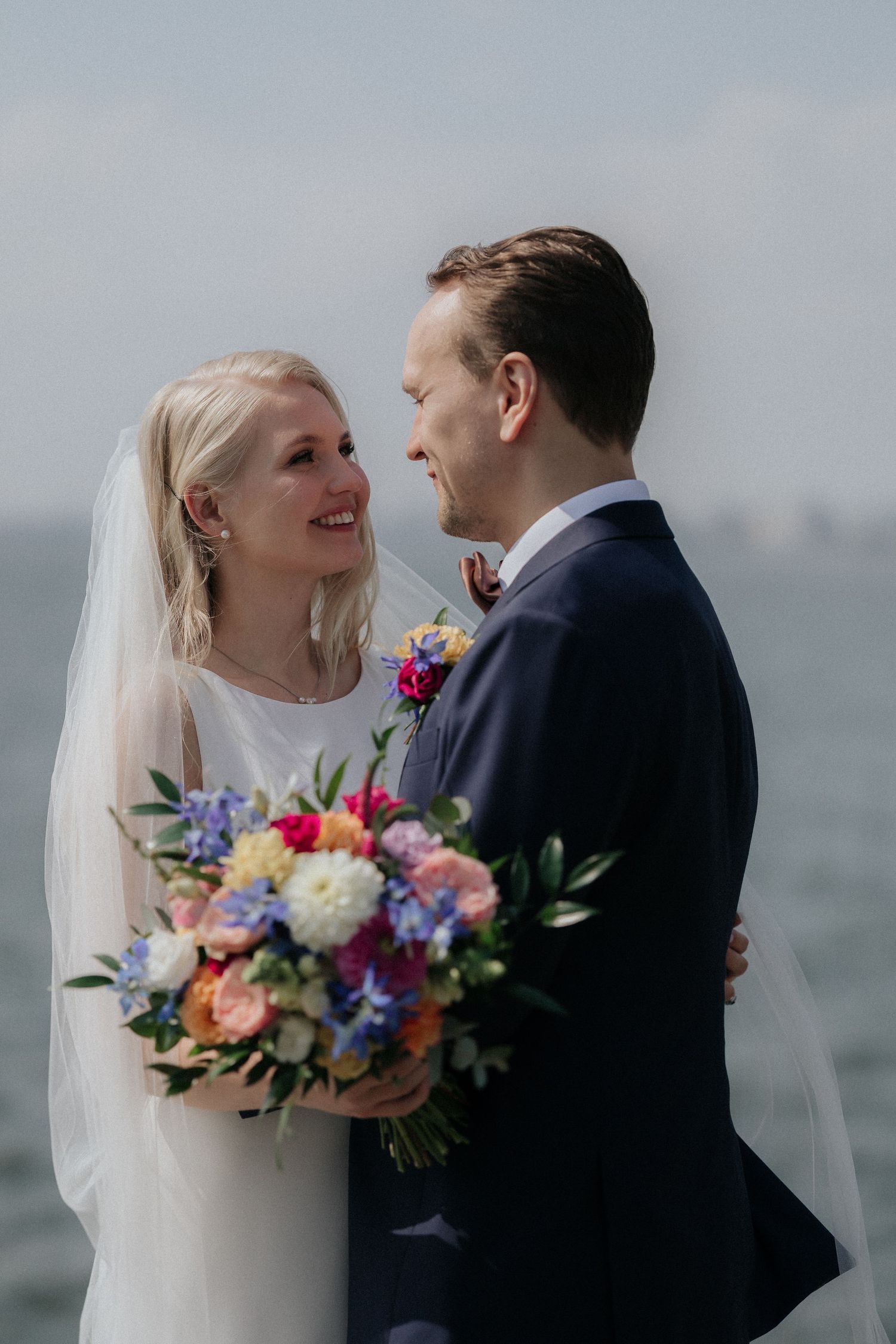 Joyful wedding couple sharing a moment, with bride holding white bouquet and groom in bowler hat.