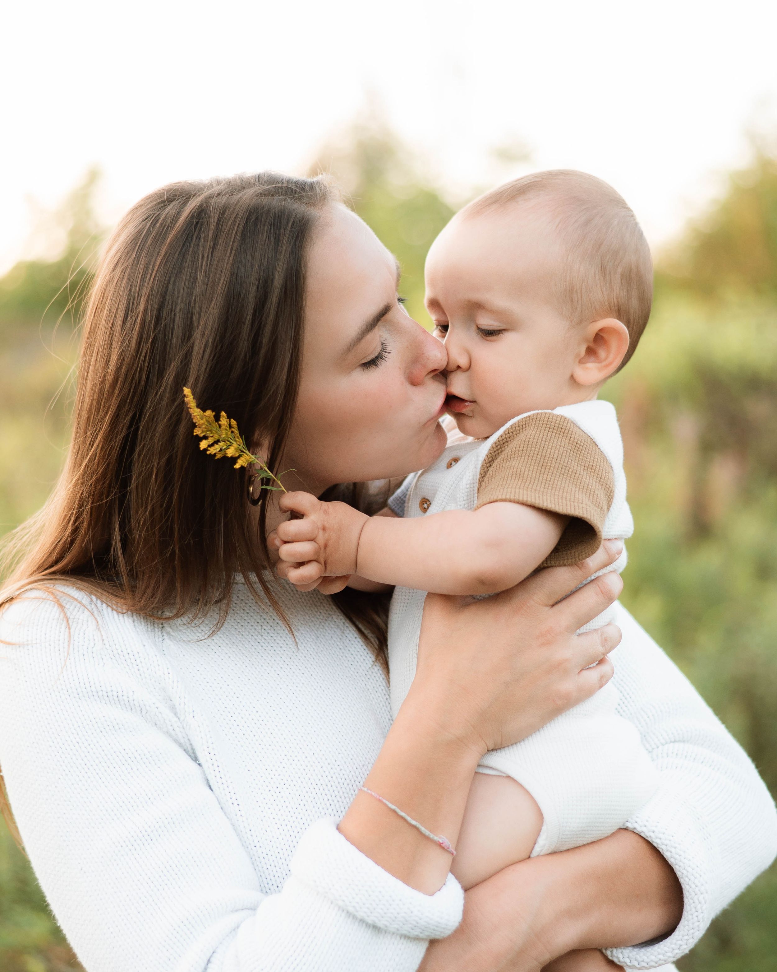Mother and baby share tender kisses and cuddles in outdoor golden hour setting.