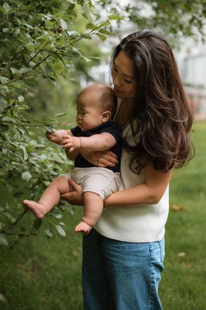 Parent and young child explore tree branches together in lush green garden setting.