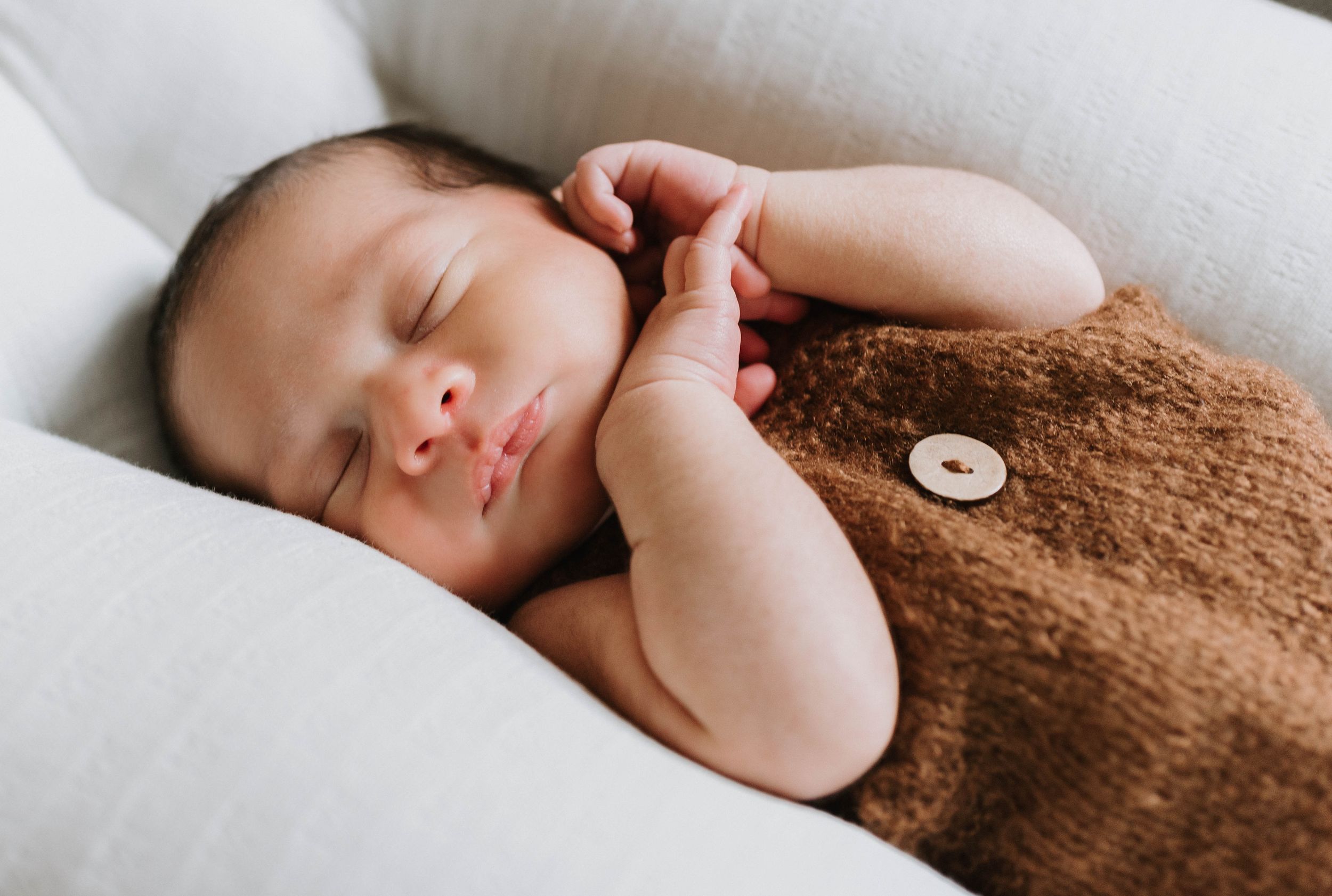 Sleeping infant wrapped in cozy brown knit blanket rests peacefully on white bedding.