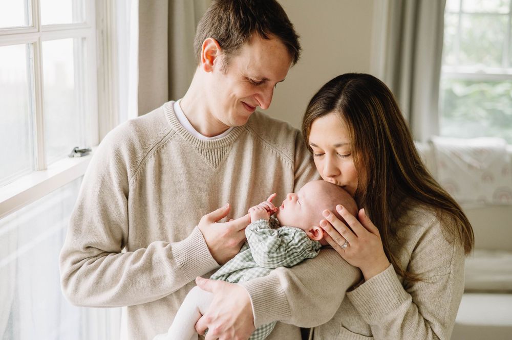A tender family moment by a bright window with a newborn baby.