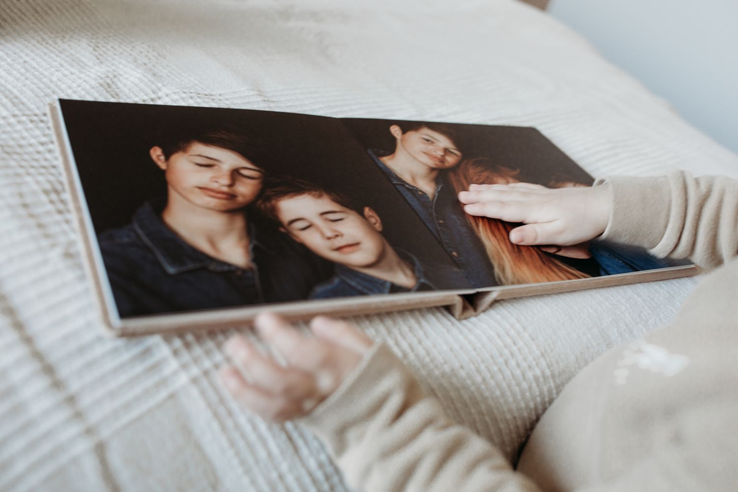 Een fotoalbum (fotoboek) die open ligt. Een kinderhand bladert door het boek en gaat met haar handje over een van de foto's.