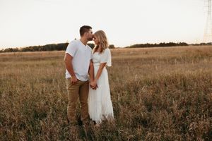 A romantic couple in white outfits embraces in a golden wheat field at sunset creating a dreamy atmosphere.