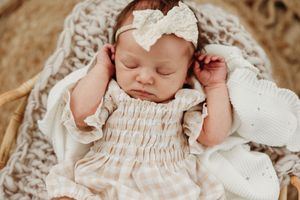 Sleeping newborn baby wearing white lace outfit and headband during professional photo session.