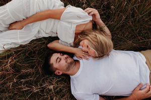Person in white dress lying peacefully in tall brown grass during golden hour photography session.
