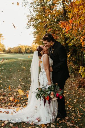 Romantic autumn wedding scene with couple embracing under colorful fall foliage as leaves scatter in the golden light.