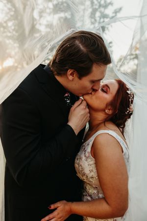 Romantic wedding couple shares a tender kiss under a dreamy veil during their intimate outdoor ceremony.
