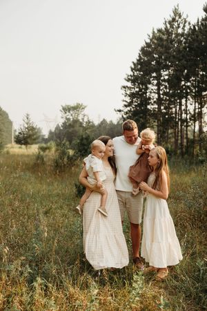 A family shares tender moments together in a sunlit meadow with tall grass and pine trees in the background.