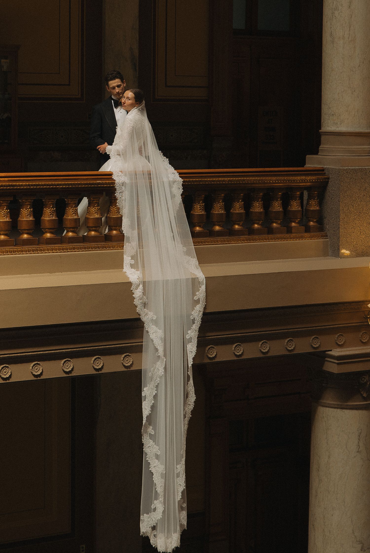 Close-up details of hands wearing elegant wedding rings against white lace dress.