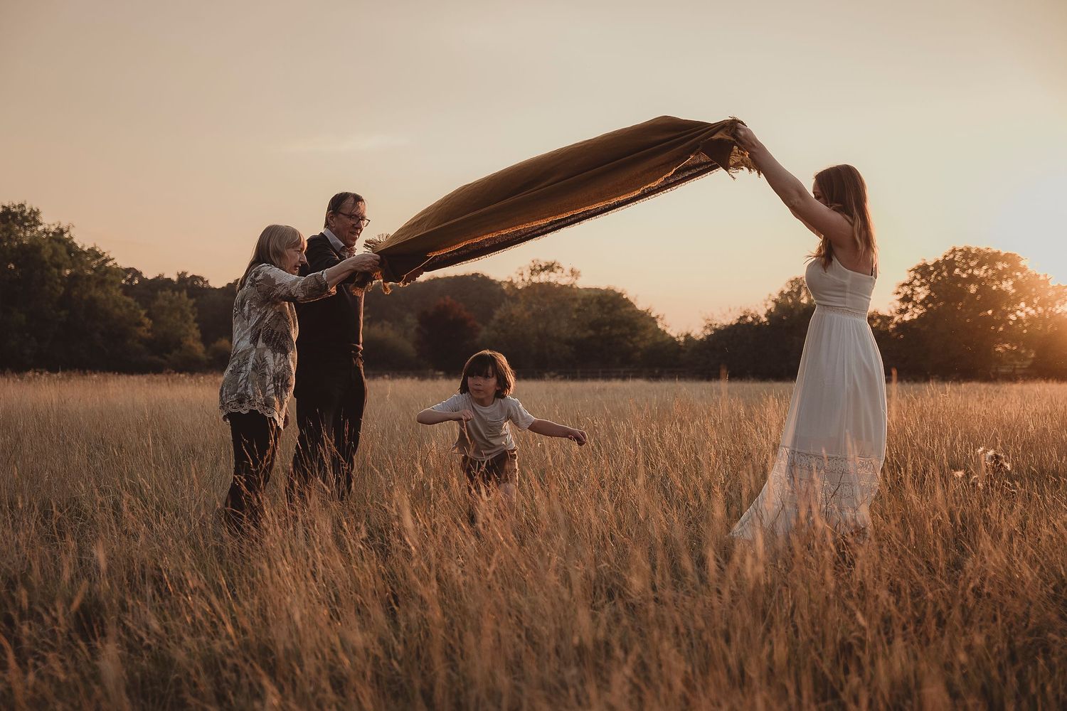 Family playing with blanket in golden wheat field during sunset photoshoot.