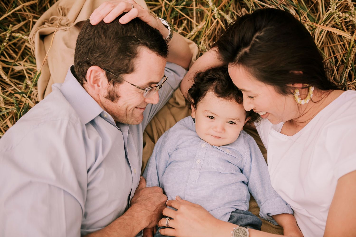 Loving family moment captured outdoors in warm sunlight while resting on hay bales.