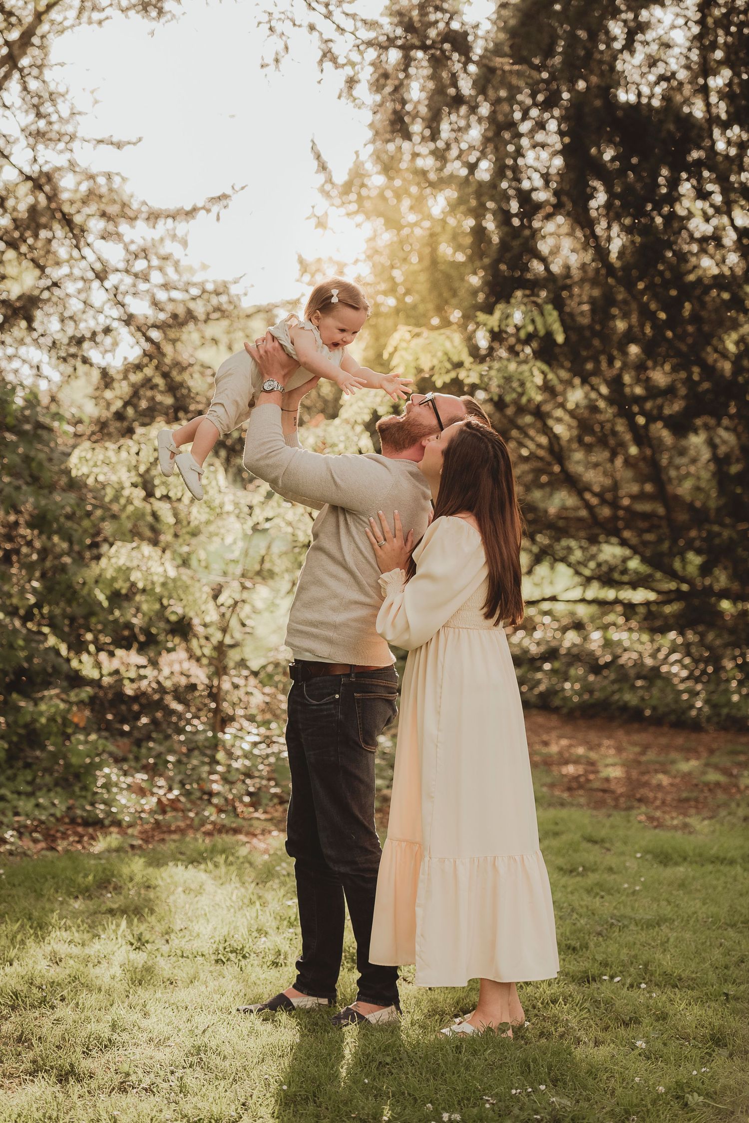 Joyful family moment captured in sunlit garden with natural backlight filtering through trees.