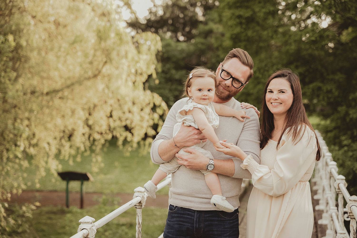 Family portrait on garden bridge in warm natural lighting.