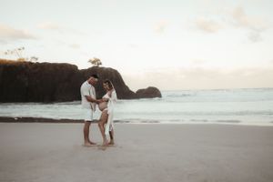 A romantic couple embraces on a scenic beach at sunset with cliffs in the background.