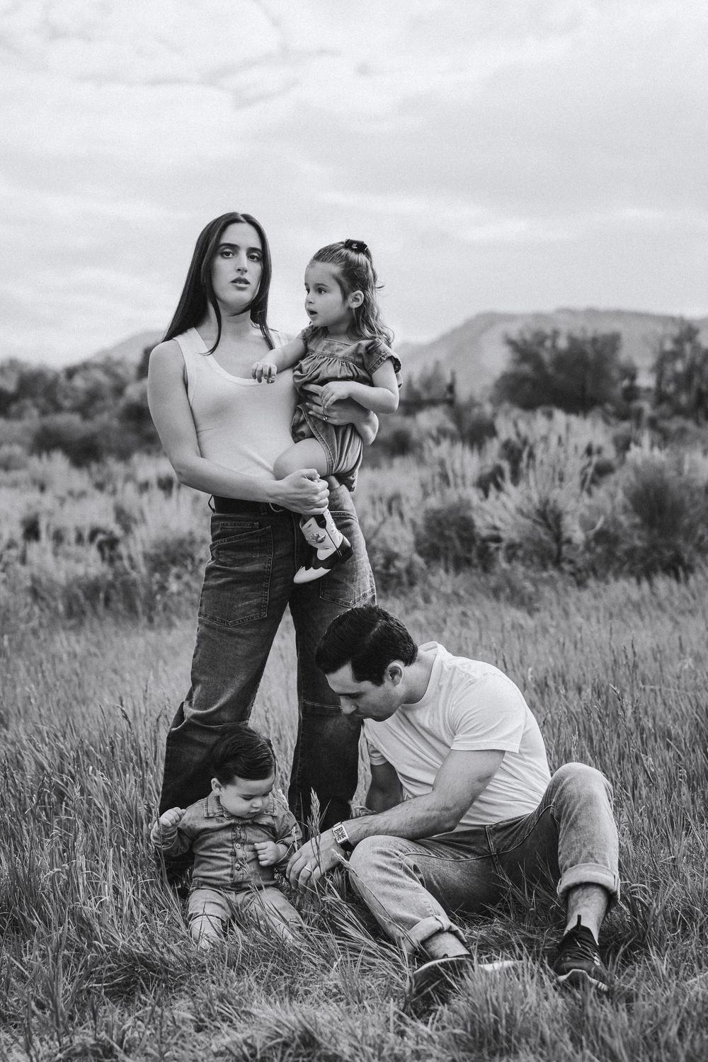 A black and white outdoor family portrait in a field with mountains in the background.