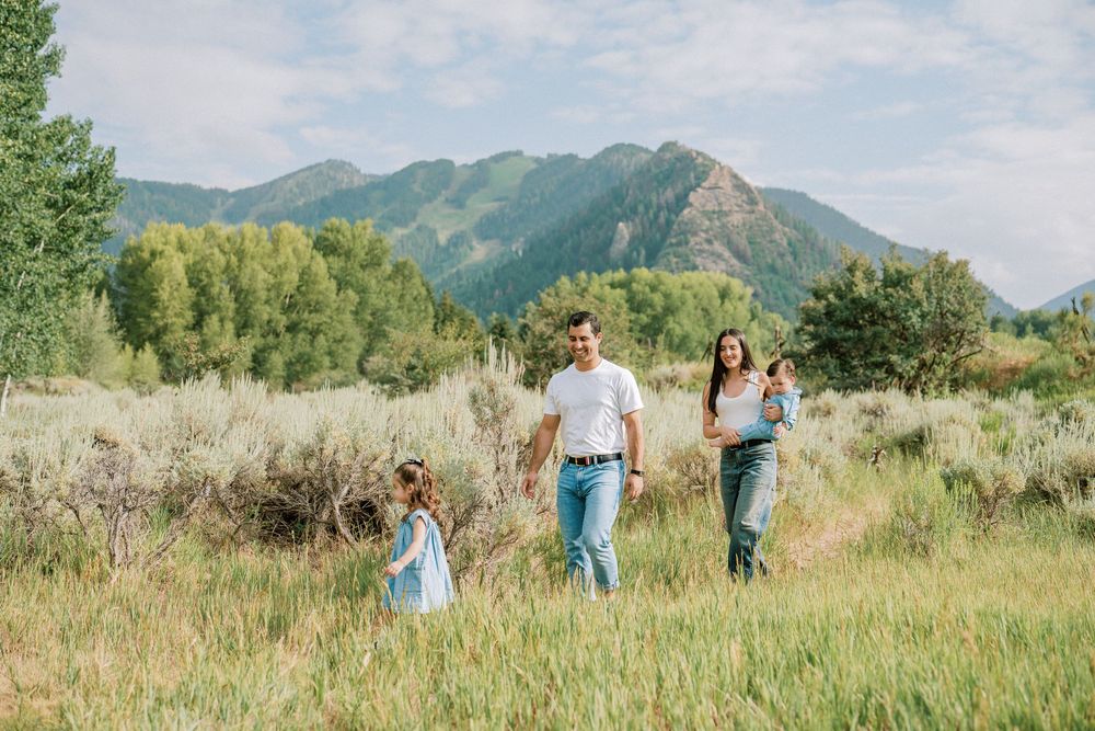 A group of people enjoying a summer day in a grassy meadow with mountain views in the background.