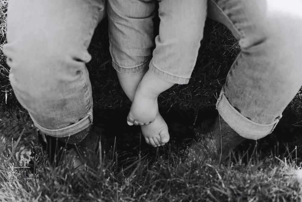 A group of people's legs and feet stand together in a circle on grass in black and white.