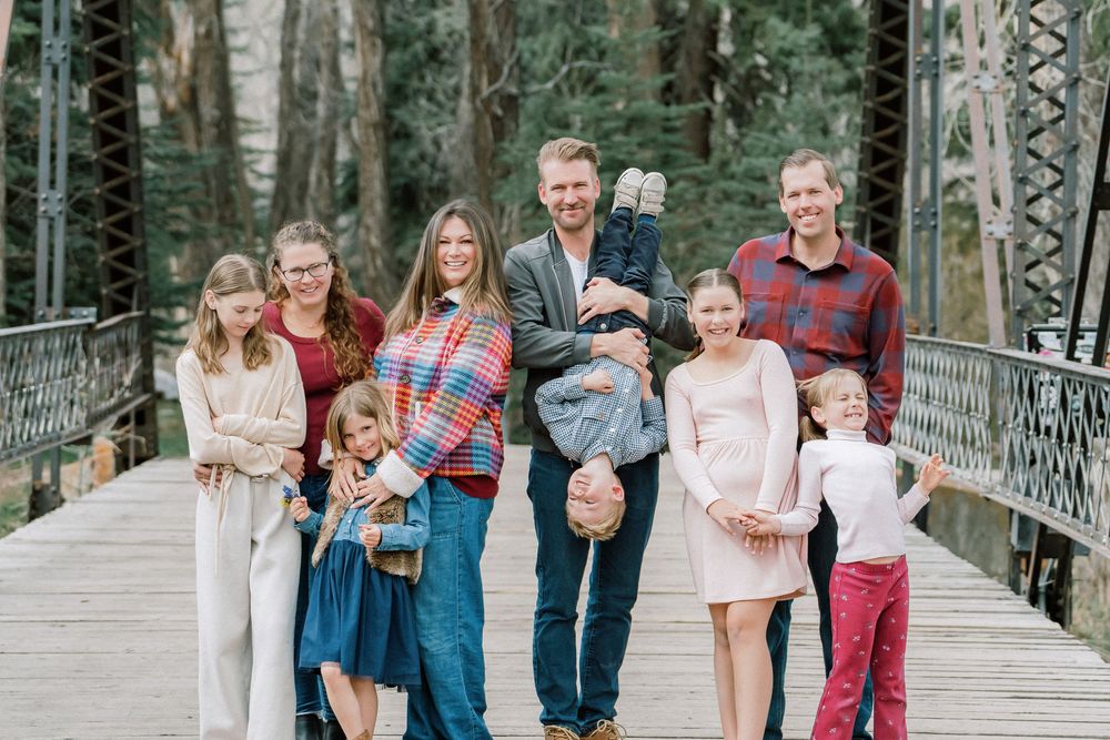 Large family posing together on a wooden bridge surrounded by trees, smiling for a portrait photo outdoors.