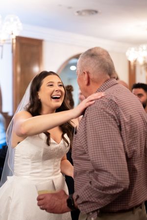 A bride in a white wedding dress shares a joyful dance with  wedding guest at the reception. Hotel Fort Des Moines Iowa wedding photography