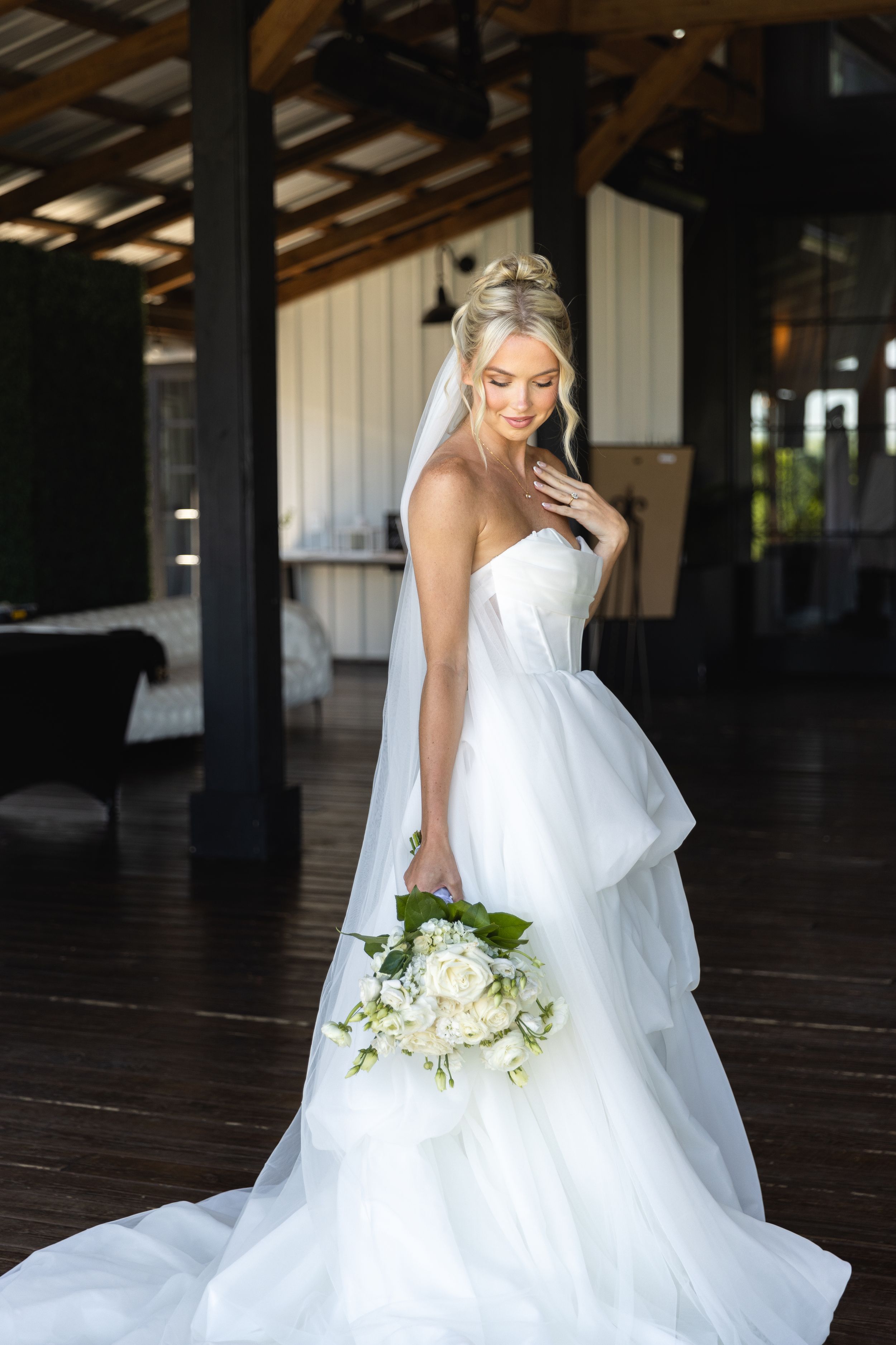 A bride in a flowing white wedding gown poses gracefully in an elegant rustic barn venue in Iowa. Posing ideas for brides in Des Moines.