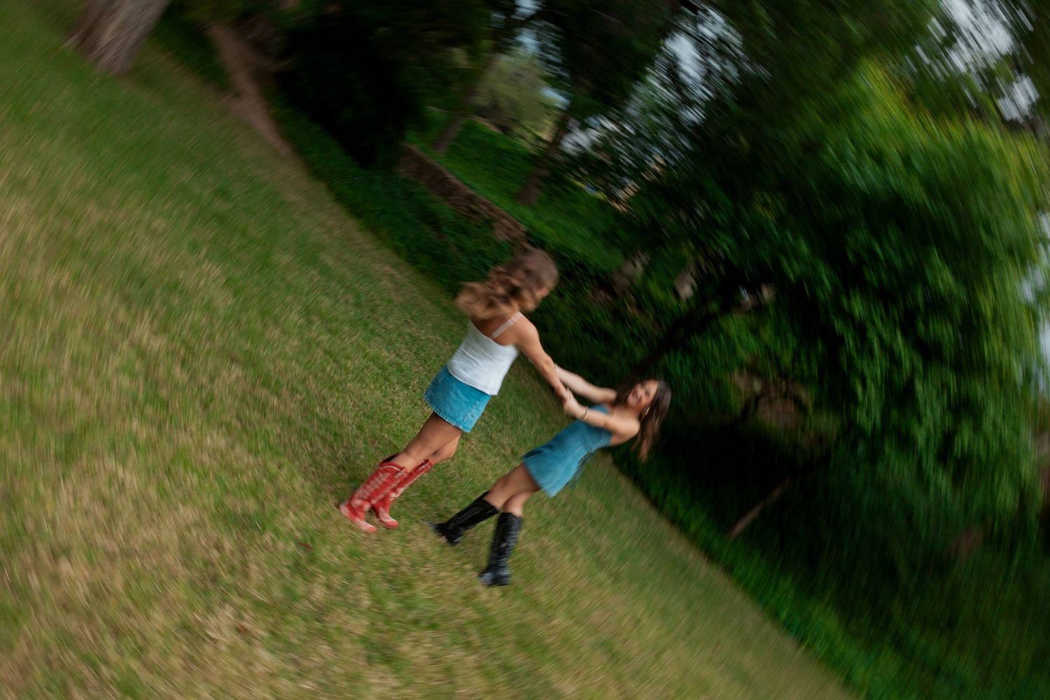 Two children spin and play together on a grassy lawn surrounded by lush green trees.