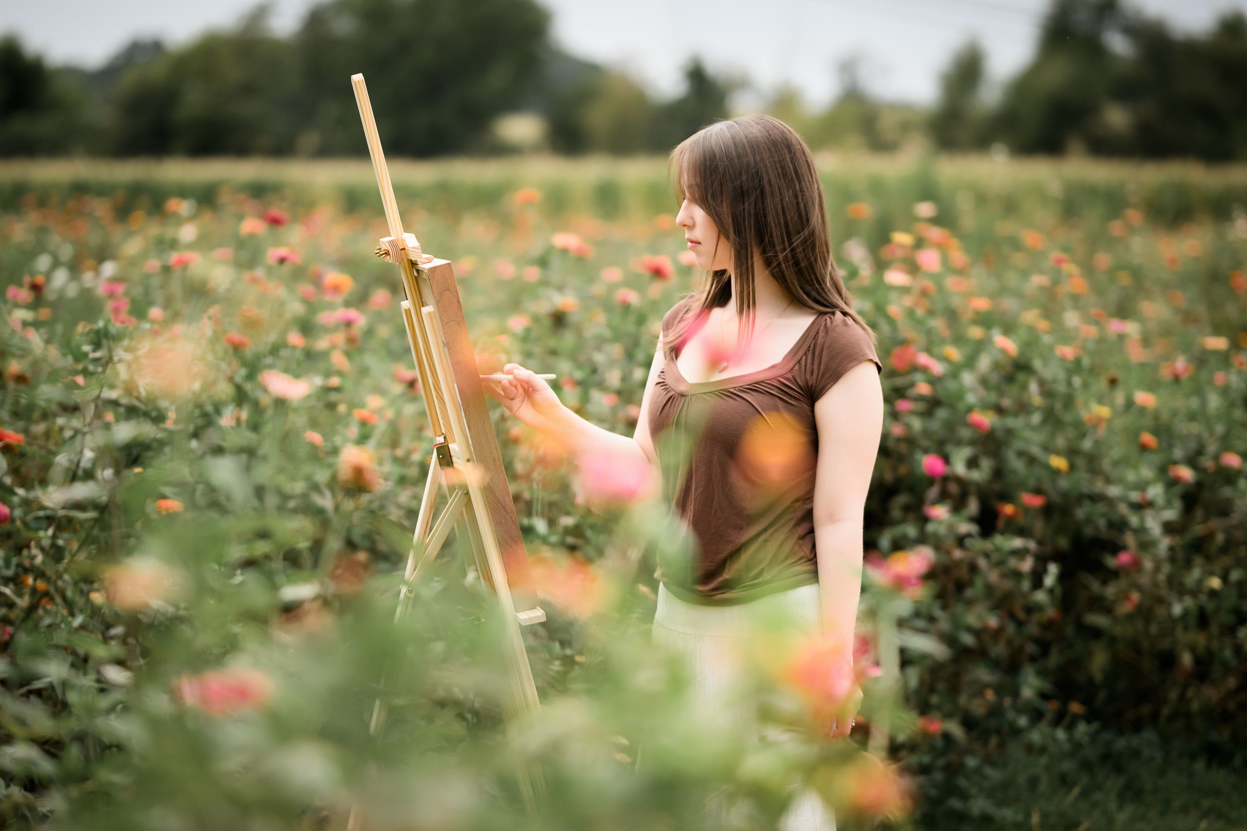 A young woman painting on an easel in a vibrant rose garden, surrounded by pink and orange blooms.