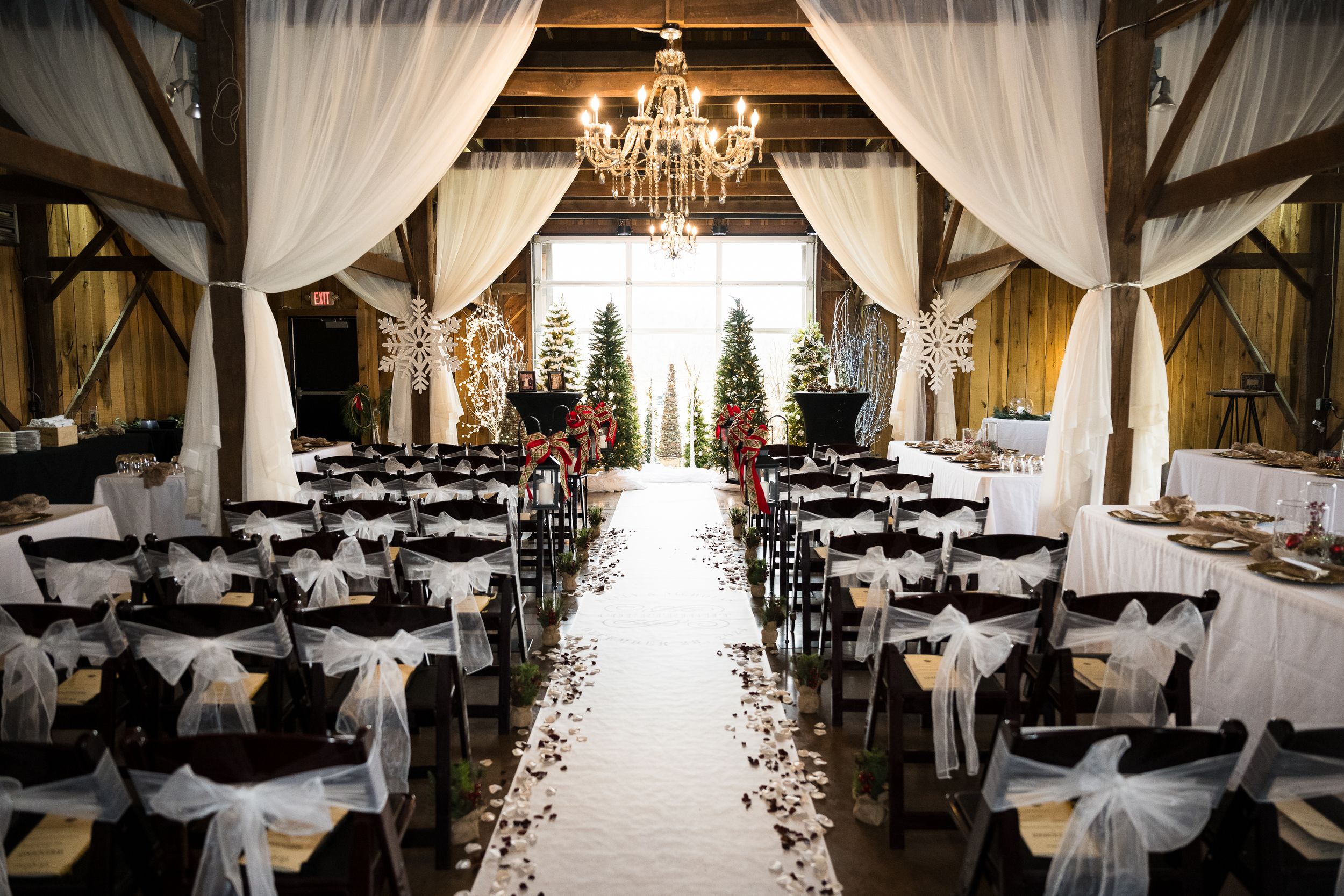 Elegant rustic barn wedding venue with white drapes, chandeliers, and rows of tables set for a reception.