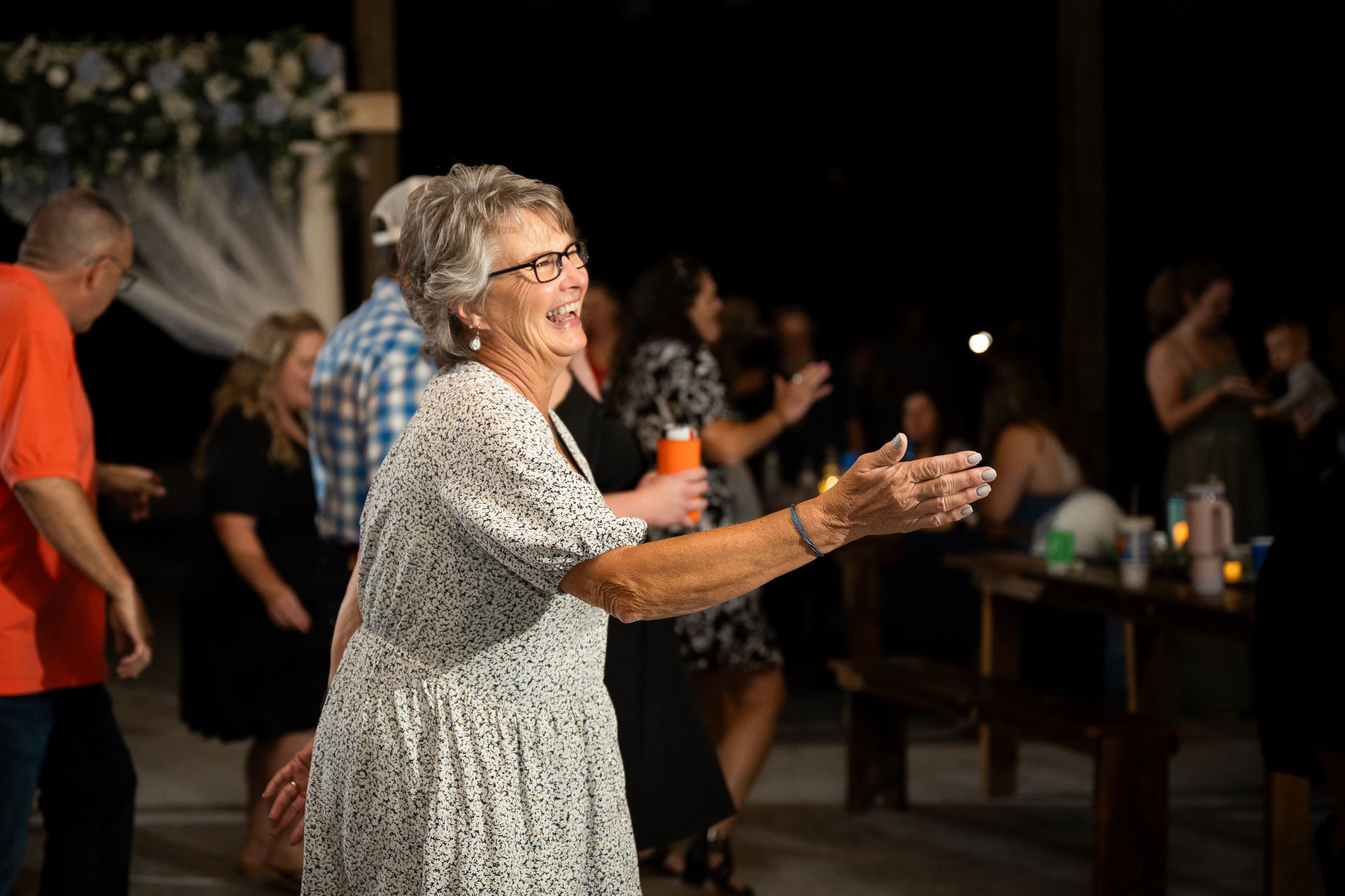 Senior woman in a sparkly dress dances enthusiastically at a party with other people in the background.