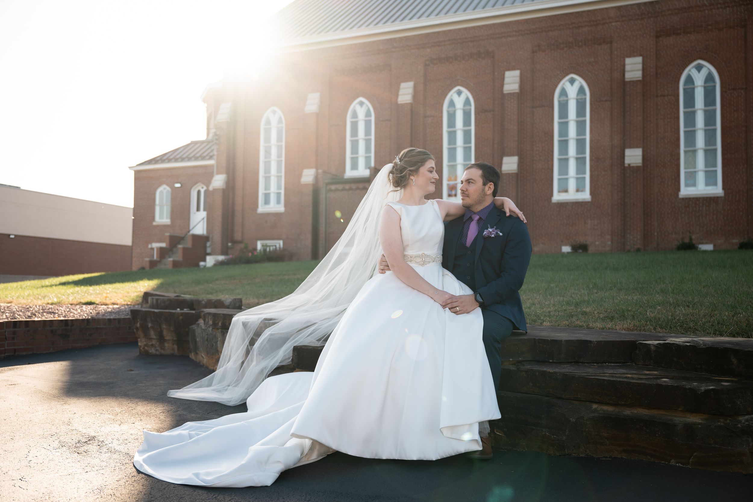 A wedding couple sits on brick steps in front of a traditional red brick church building.