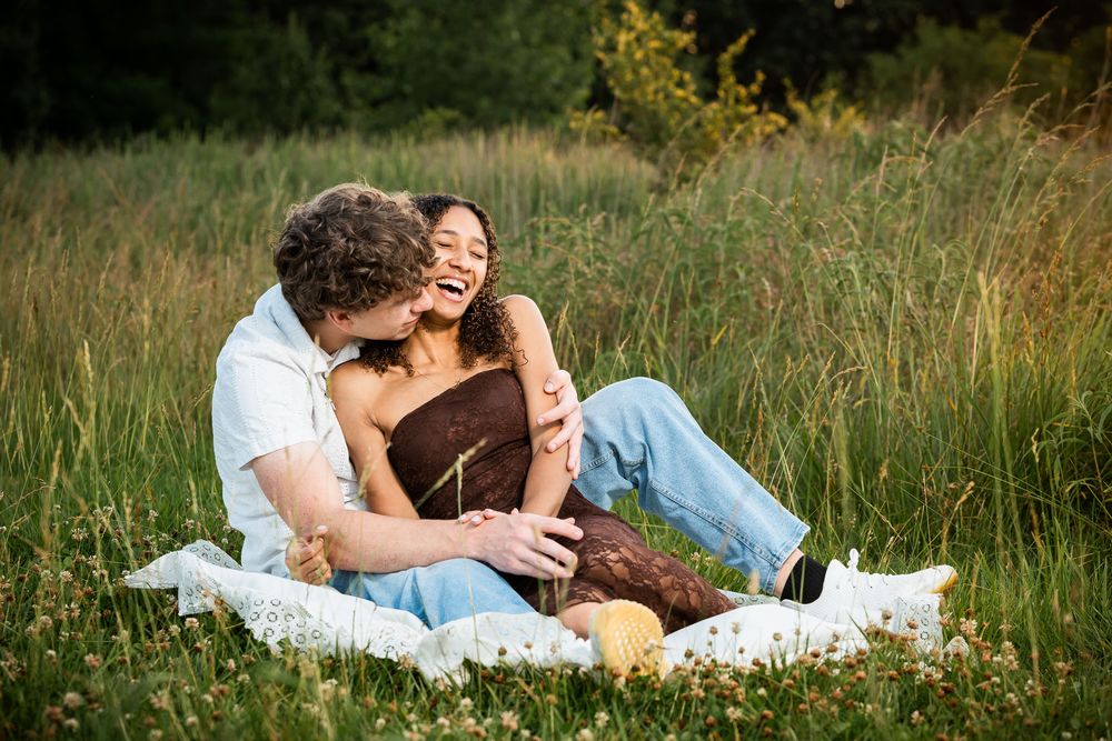 Happy couple laughing together on a picnic blanket in a sunny meadow.