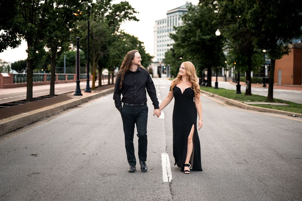A couple walking together down a tree-lined urban street in casual attire.
