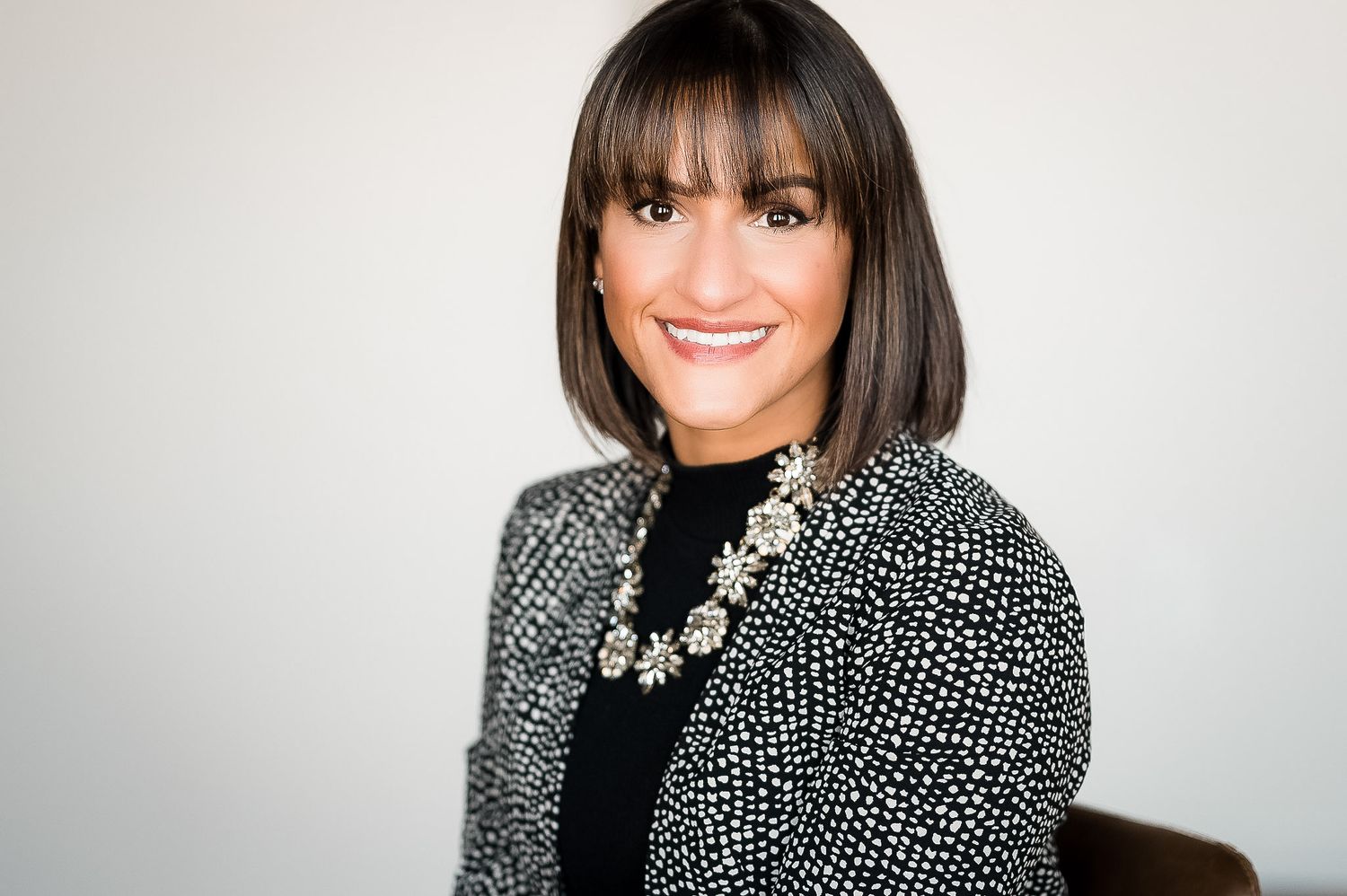 Professional headshot of someone wearing a black and white patterned blazer with a statement necklace against light background.