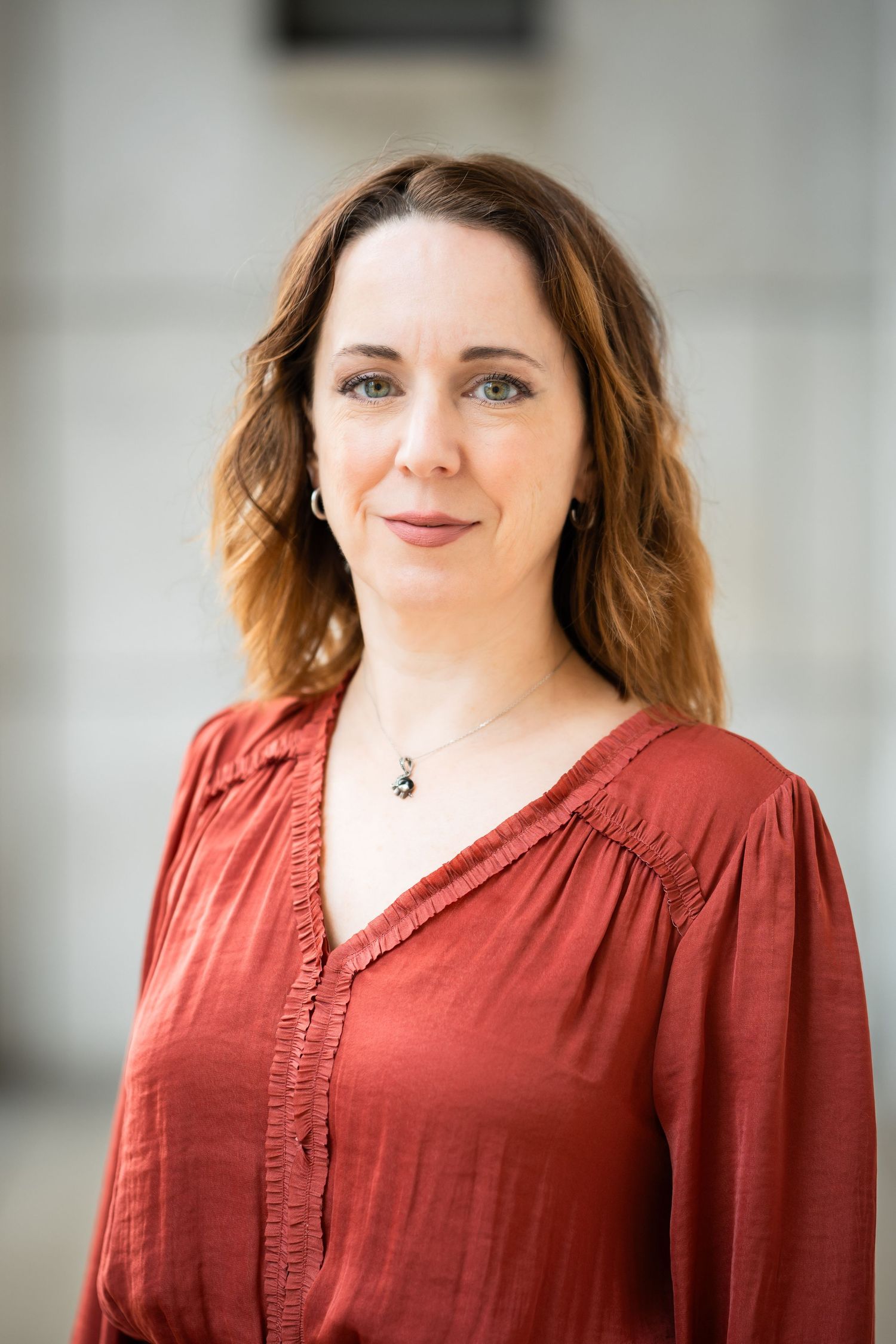 Professional headshot portrait of someone in a rust-colored blouse smiling warmly against a light background.