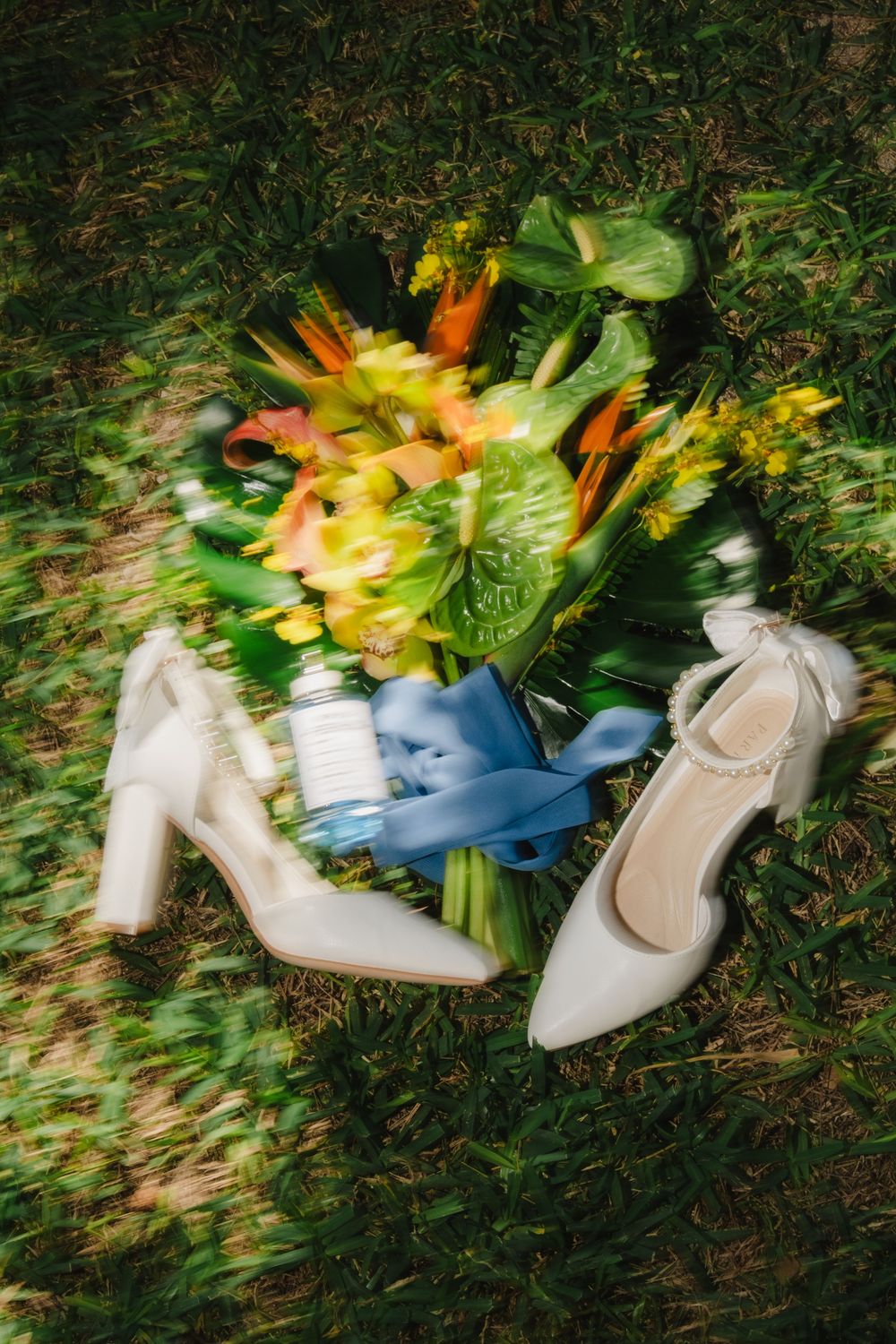White wedding shoes with floral bouquet arranged on grass in natural outdoor lighting.