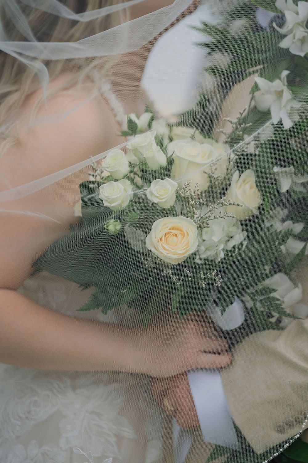 Close-up details of white and cream wedding bouquets with roses and delicate greenery against a light background.
