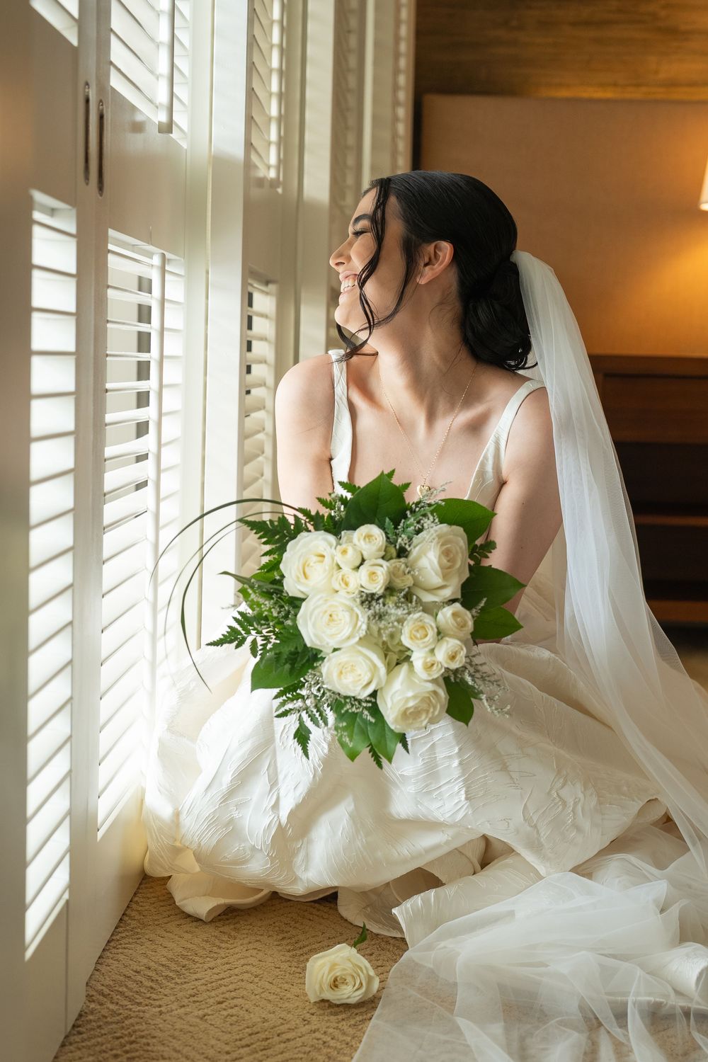 A bride in a white wedding gown poses near window shutters getting ready  Wedding at the Four Seasons Resort Oahu