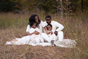 Happy Black family of four dressed in white sitting on a blanket in a scenic autumn field.