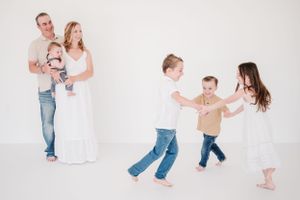 A playful family photo session with everyone wearing casual attire in a white studio.