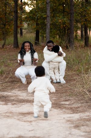Happy Black family in matching white outfits playing outdoors in autumn forest, parents embracing children on dirt path.