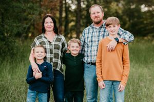 A casual family portrait taken outdoors in a grassy field during golden hour.