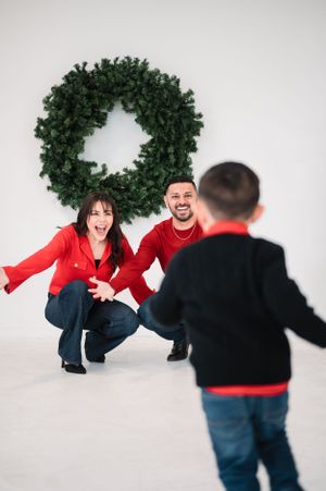 Candid family moments captured against white studio backdrop with holiday wreath decoration.