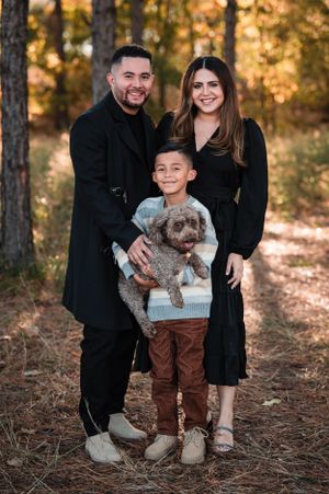 A family poses with their fluffy dog among fall trees at sunset.