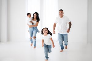 Playful family photoshoot in a minimalist white studio setting wearing casual denim and white outfits.