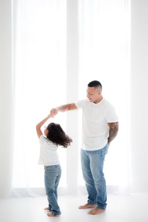 Playful family photo session against white backdrop showing fun interactions in casual white and denim outfits.