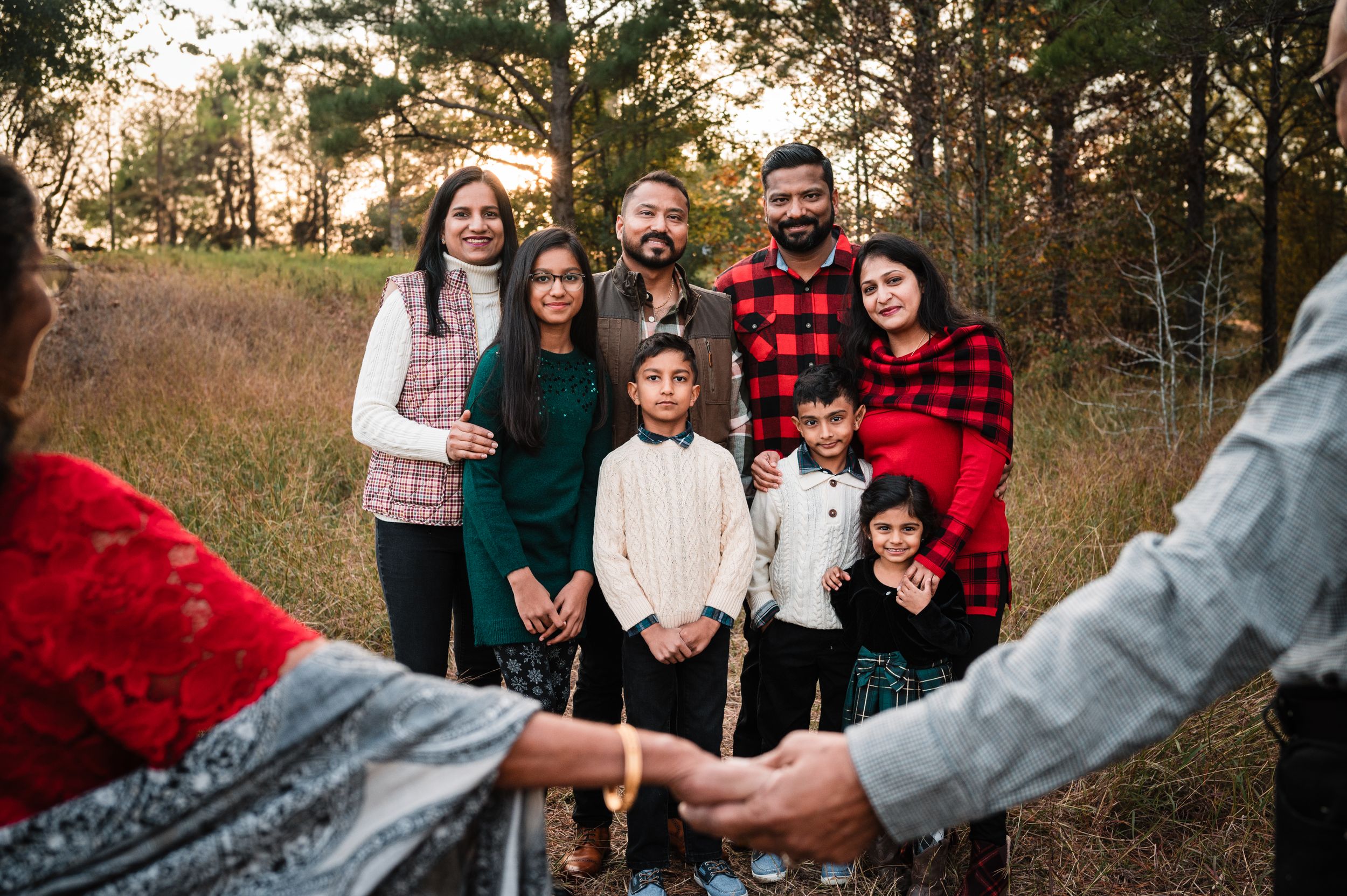 Family wearing coordinated winter outfits poses together in a wooded setting.