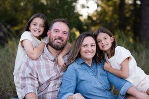 Happy family of four smiling outdoors, parents with two young daughters in a natural green setting.